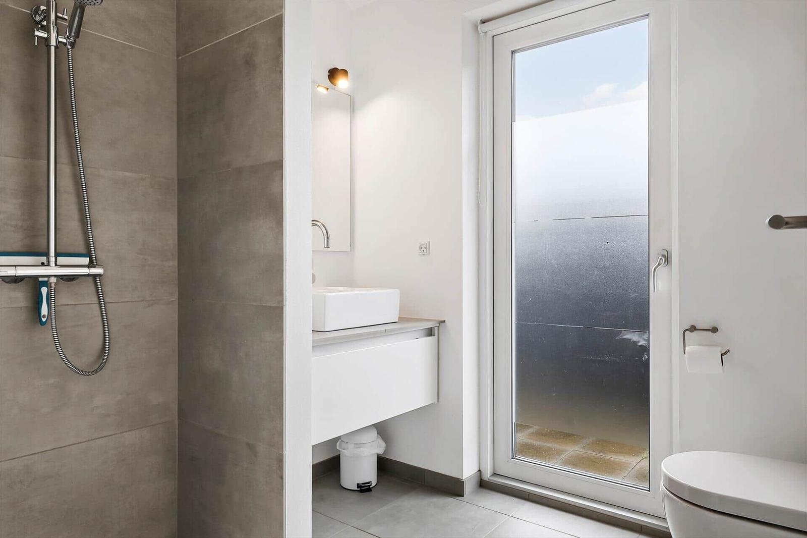 Bathroom with shower, sink, and toilet. Large glass door leads to balcony.
