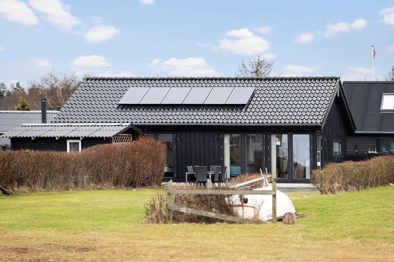 Black house with solar panels and terrace. Lawn and white boat in the foreground.
