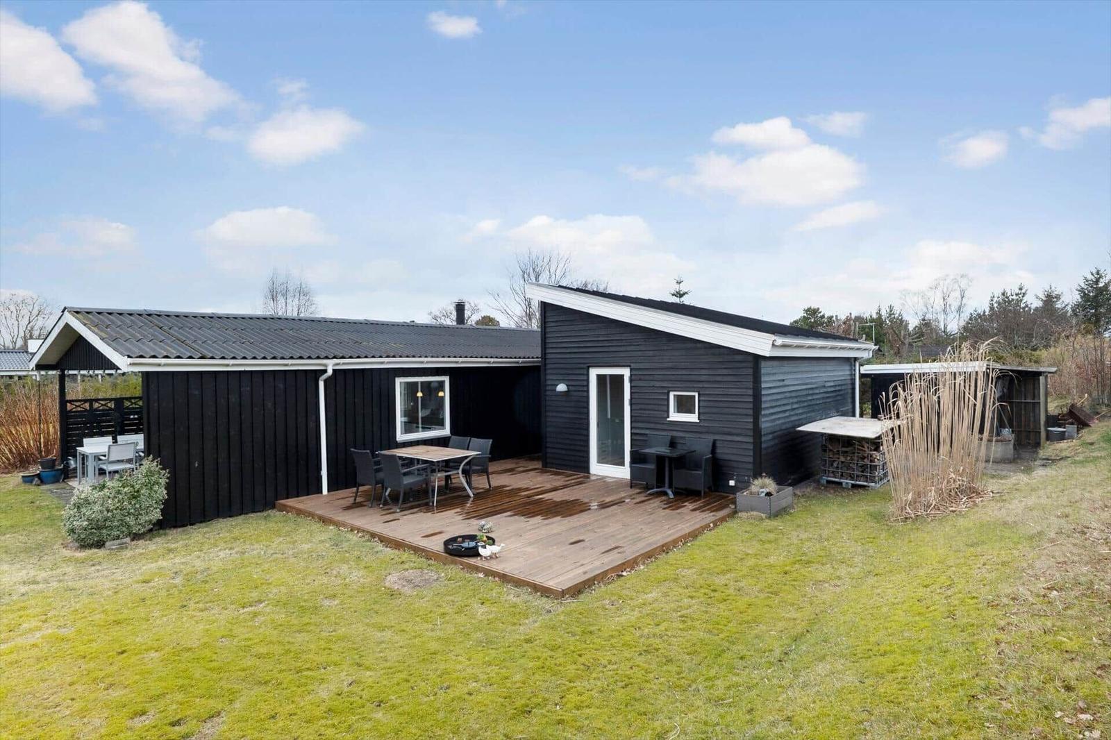 Schwarzes Haus mit Holzterrasse und Garten. Außentisch, Sitzgelegenheiten und Grillmöglichkeit.