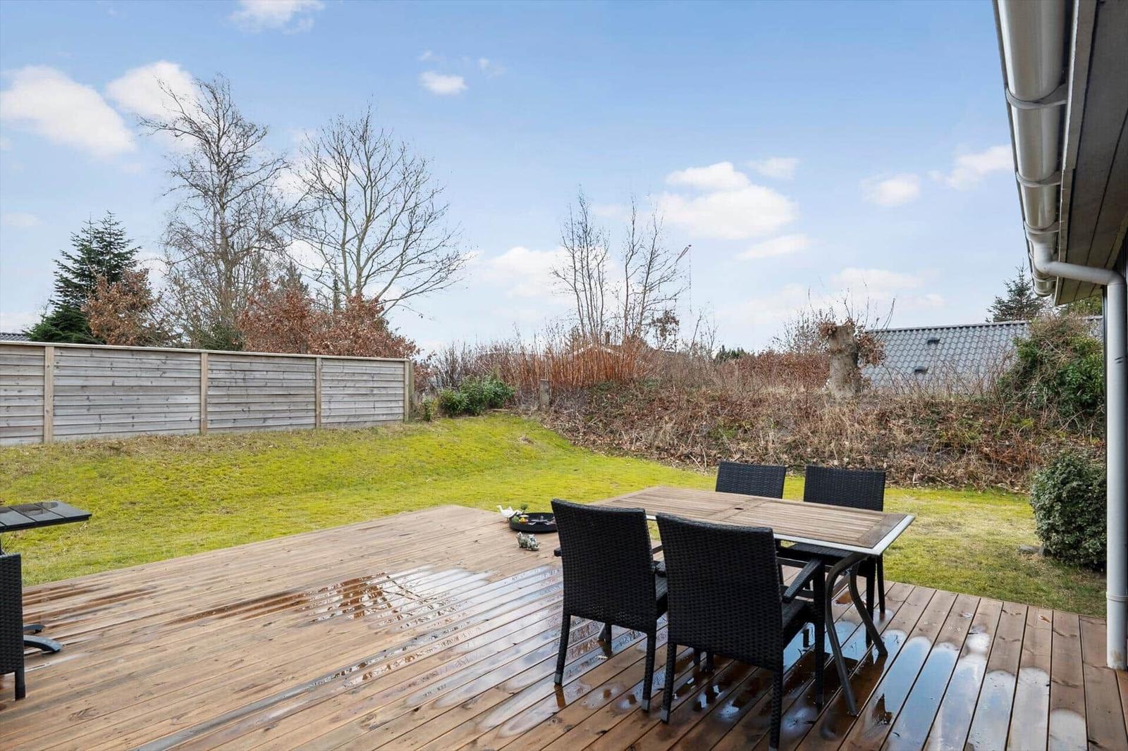 Terrasse mit Tisch und Stühlen, grüner Rasen und Zaun im Hintergrund.