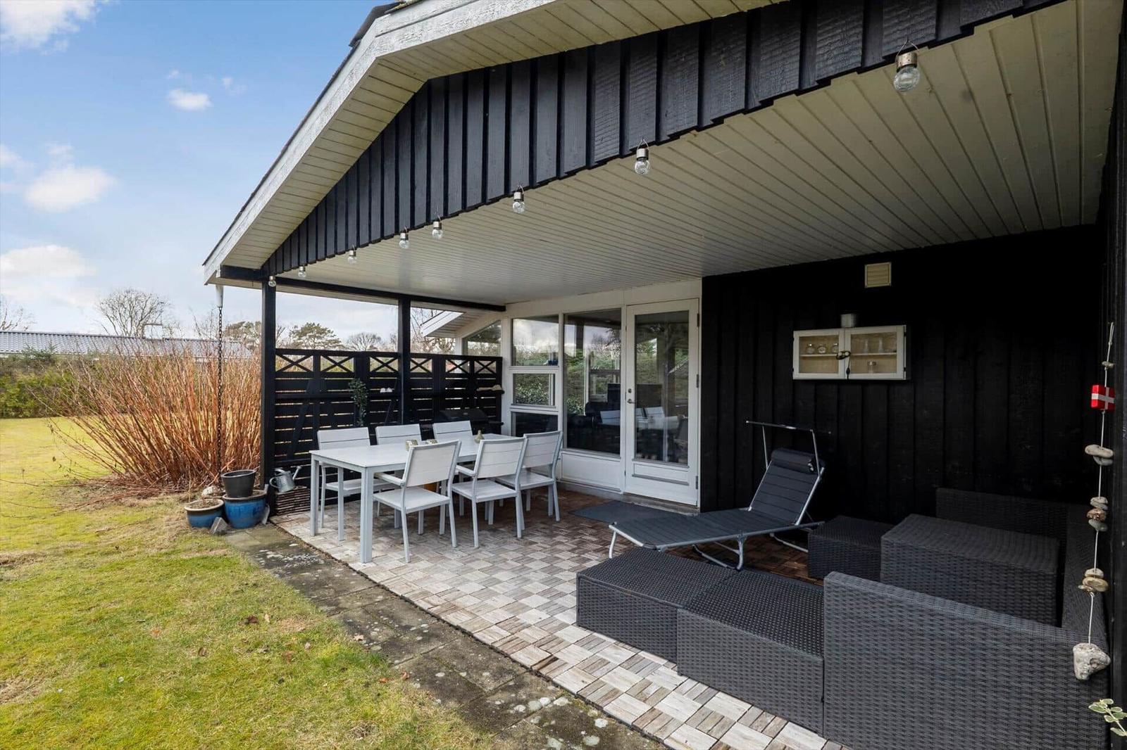 Terrasse mit Tisch, Stühlen und Liege. Schwarze Holzwände und Glasfront.