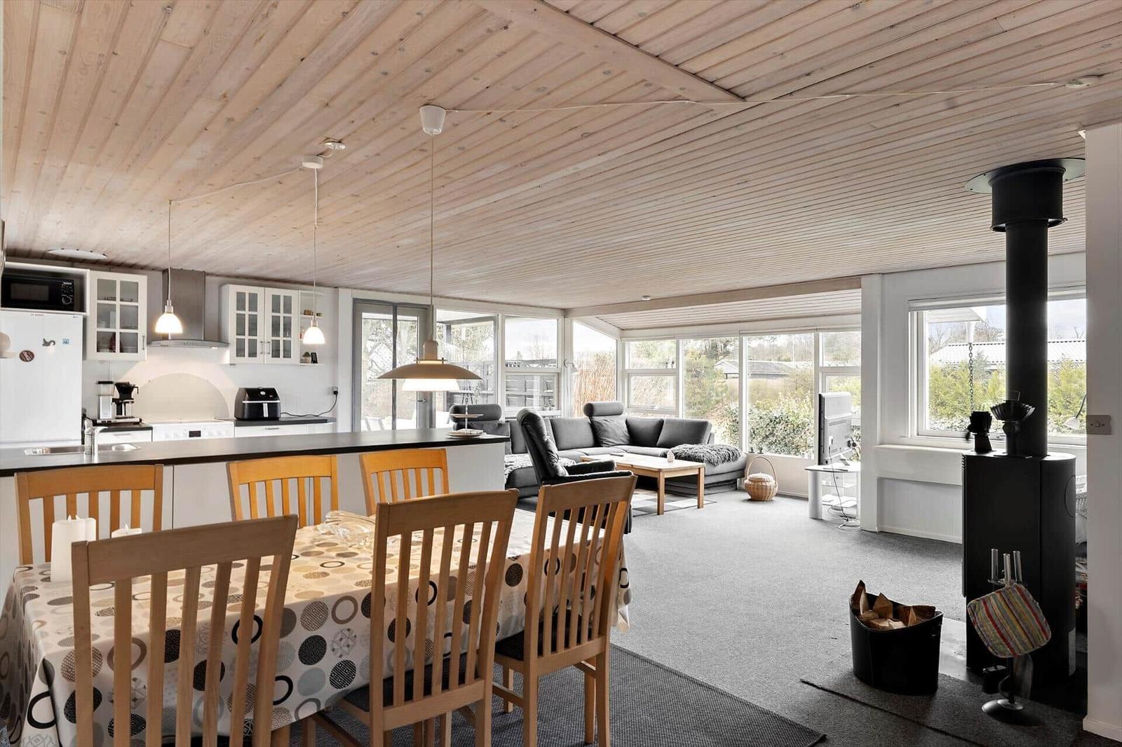 Offener Raum mit Küche, Essbereich und Wohnzimmer. Holzdecke, Fenster und Kamin.
