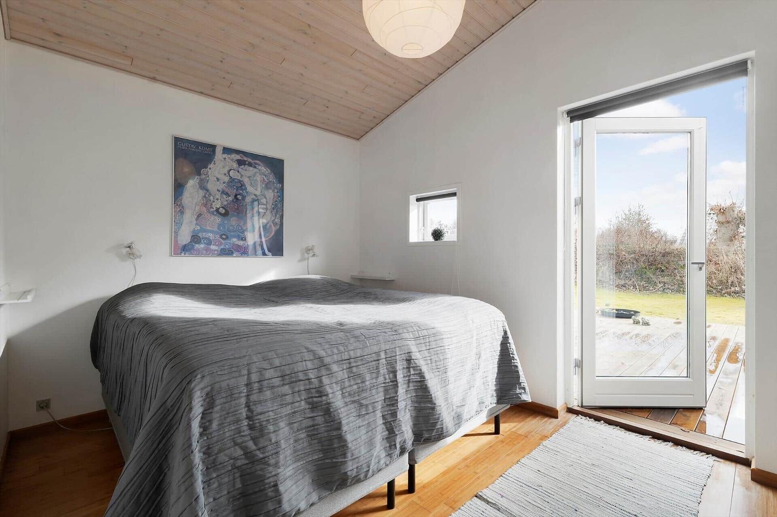 Schlafzimmer mit Bett, Decke und Tür zu einer Terrasse.