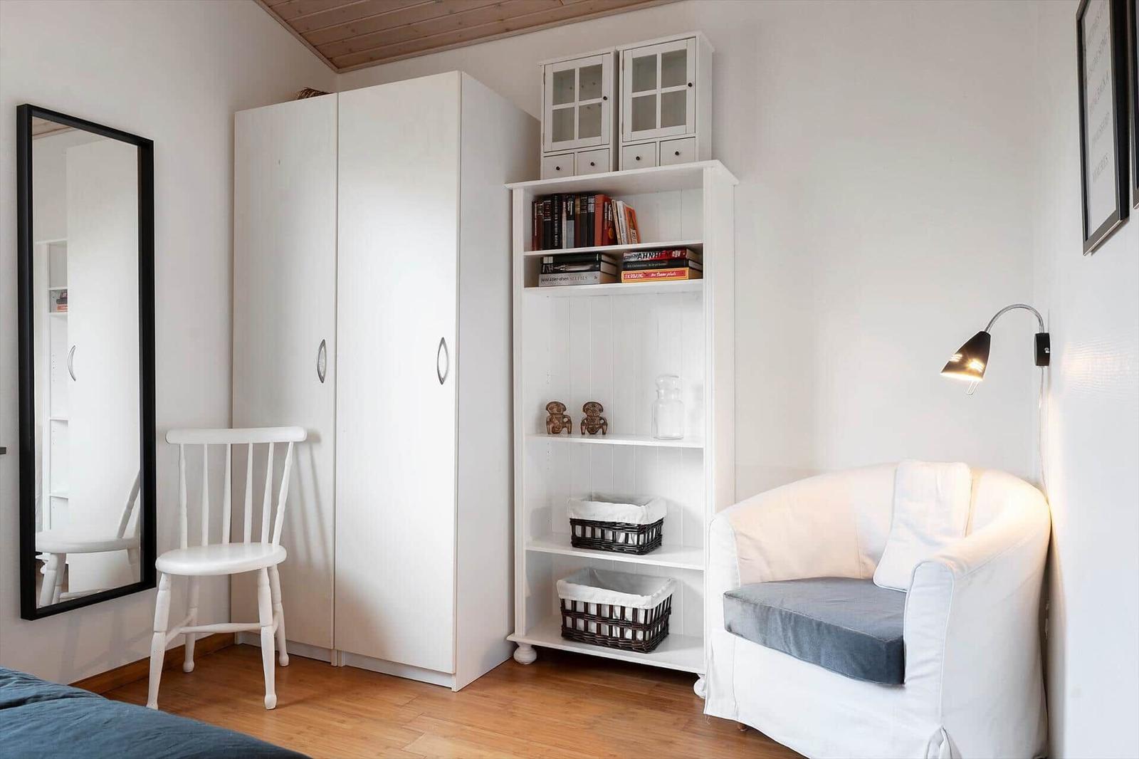 Schlafzimmer mit weißen Schränken, Sessel und Bücherregal.