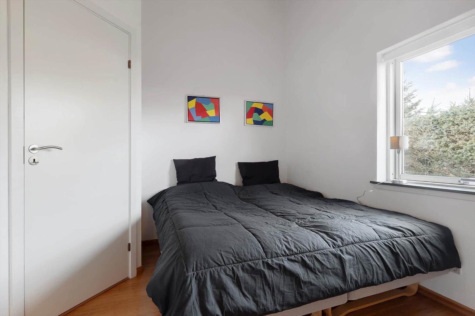 Schlafzimmer mit Bett, Fenster und zwei Bildern an der Wand.
