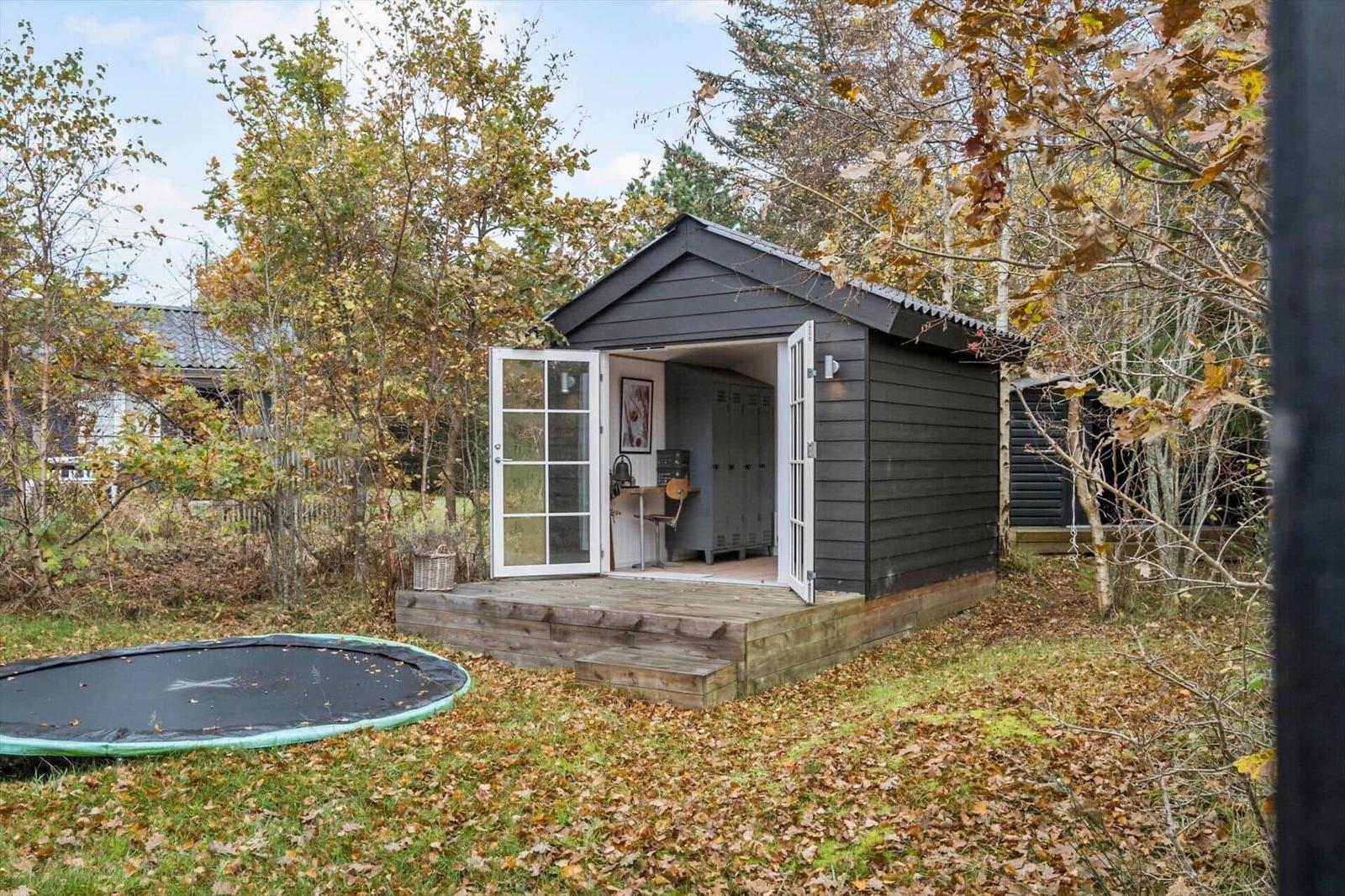 Ein kleines schwarzes Haus mit offenen Türen und einem Trampolin im Herbst.