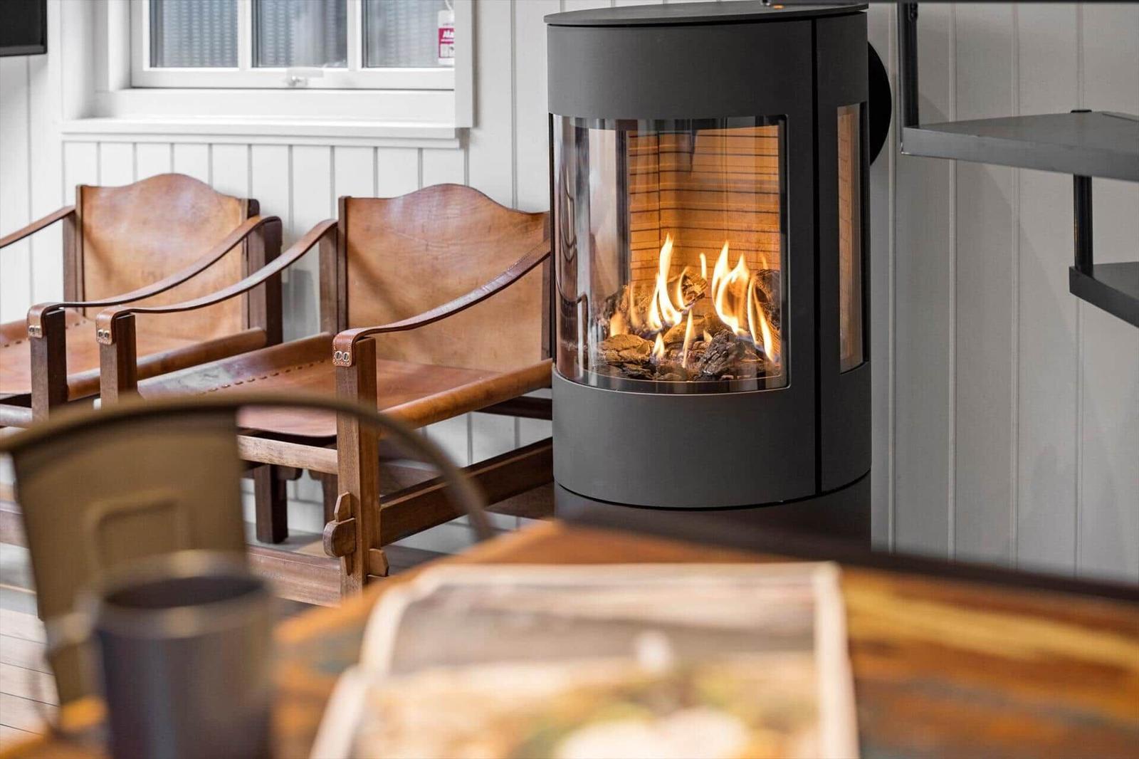 Ein Kamin mit brennendem Holz steht neben zwei Ledersitzen. Hintergrund: weiße Paneelen.