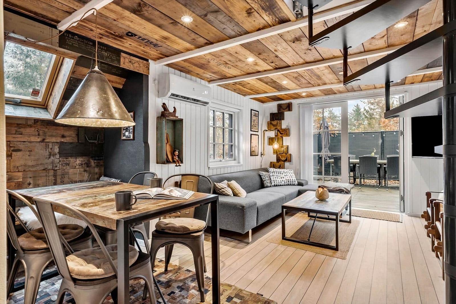 Wohnraum mit Essbereich, Sofa und Holzdecke. Durchgang zur Terrasse mit Garten.