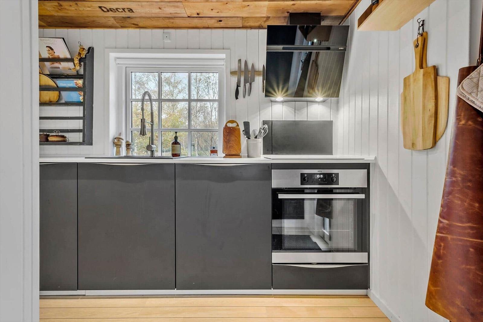 Küche mit dunklen Schränken, Herd und Fenster mit Blick auf Bäume.