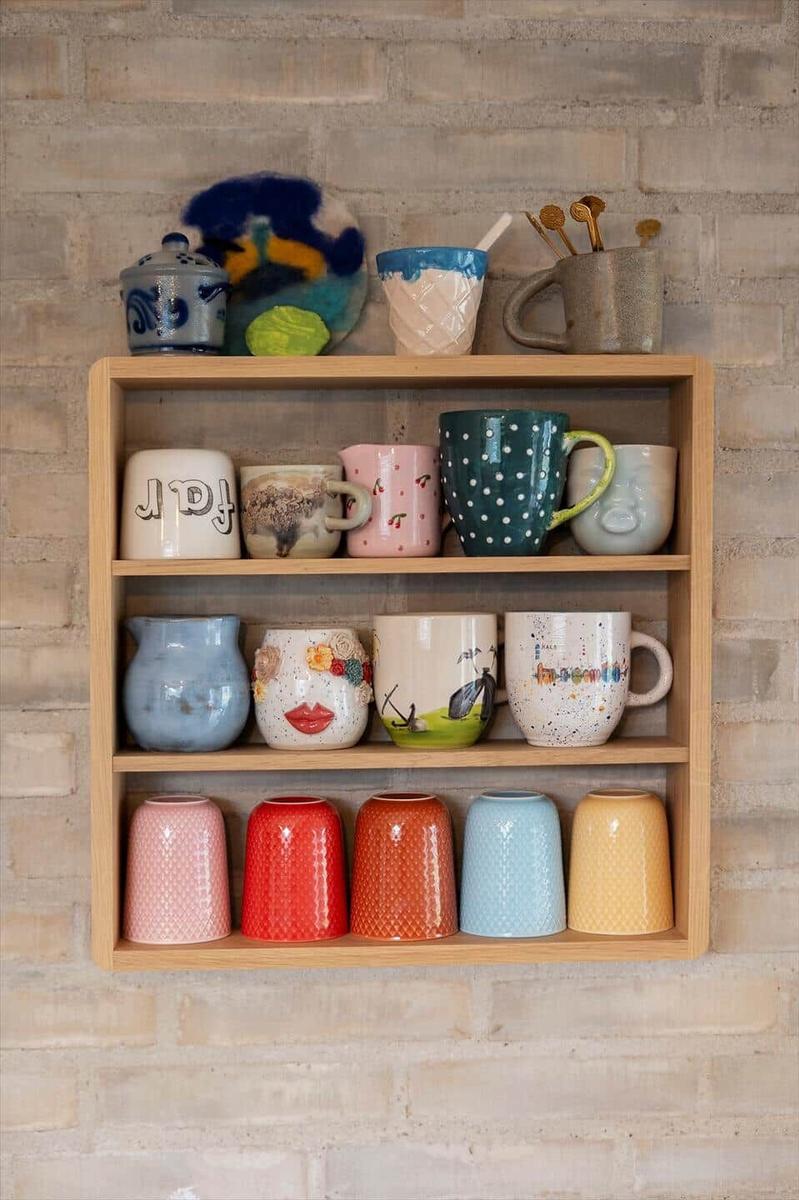 Wooden shelf with colorful mugs against brick wall