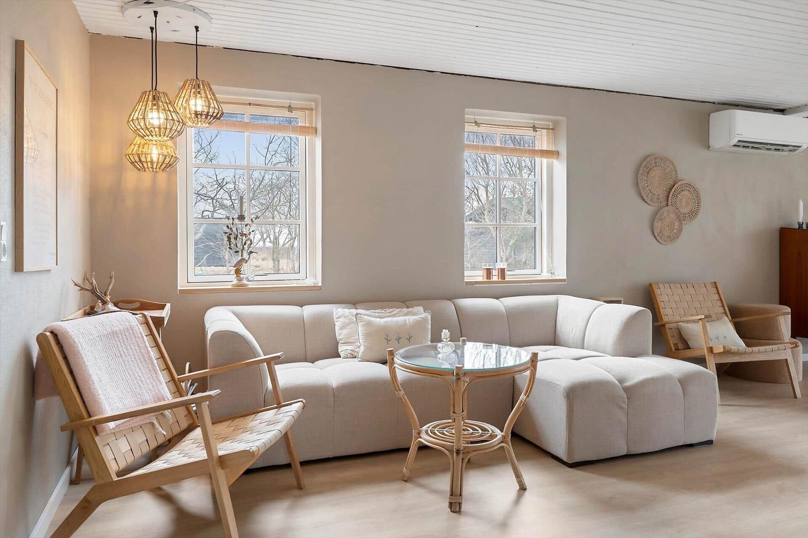 Living room with sofa, chairs, and table. Two windows, ceiling lights, and wall decor.