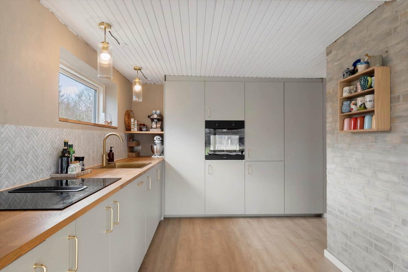 Modern kitchen with wooden surfaces and built-in oven. Shelf with mugs on brick wall.