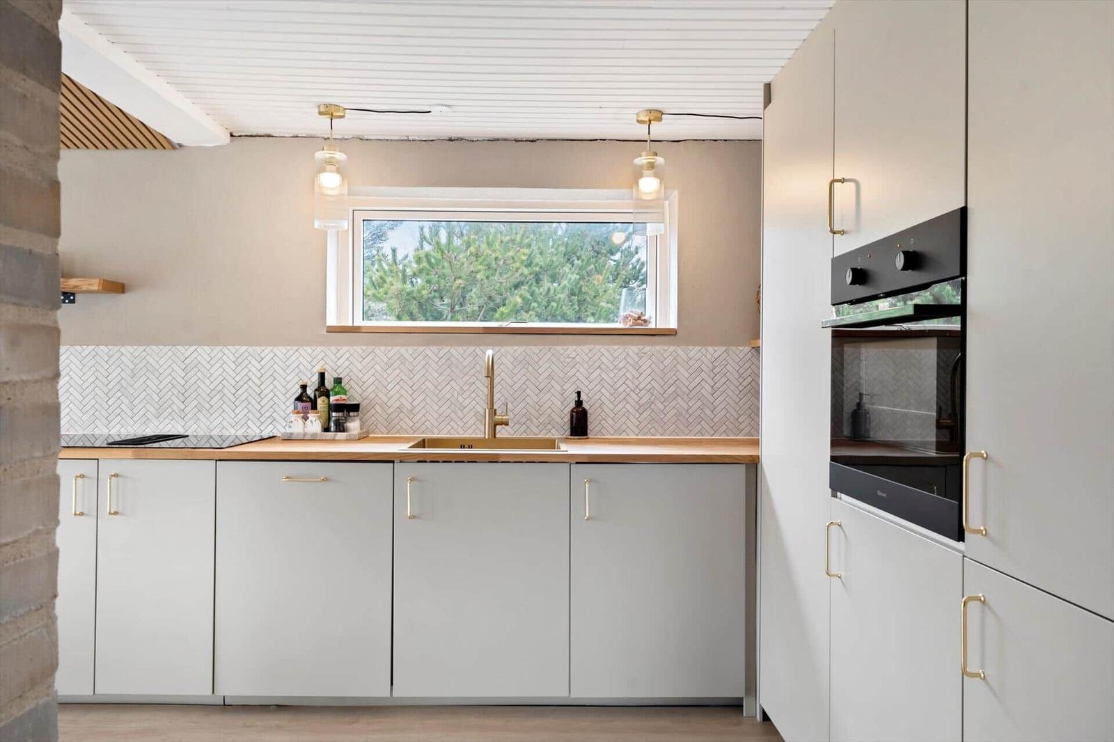 Modern kitchen with worktop, sink and window. White cabinets and backsplash with mosaic.