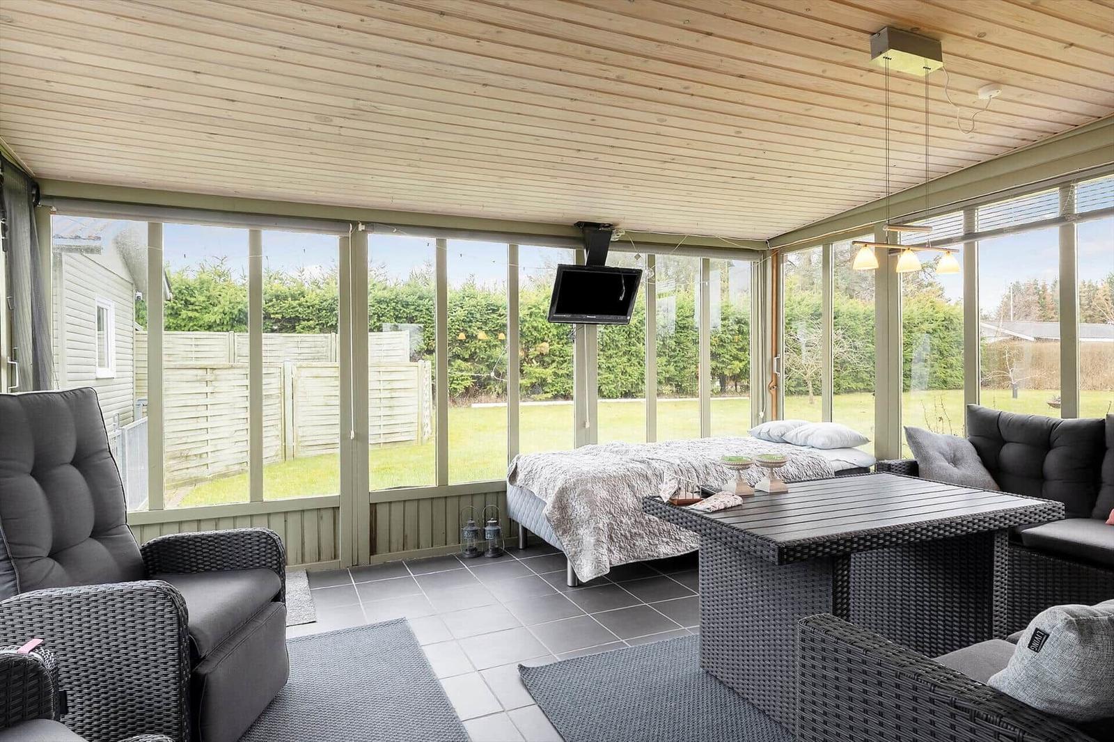 Sun terrace with sleeping area, seating group, and TV. View of garden and fence.