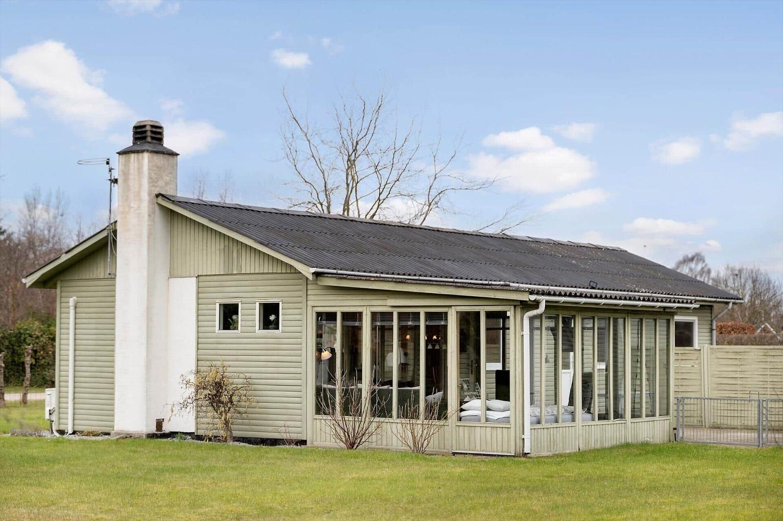 A house with large glass front and green fence in the garden.