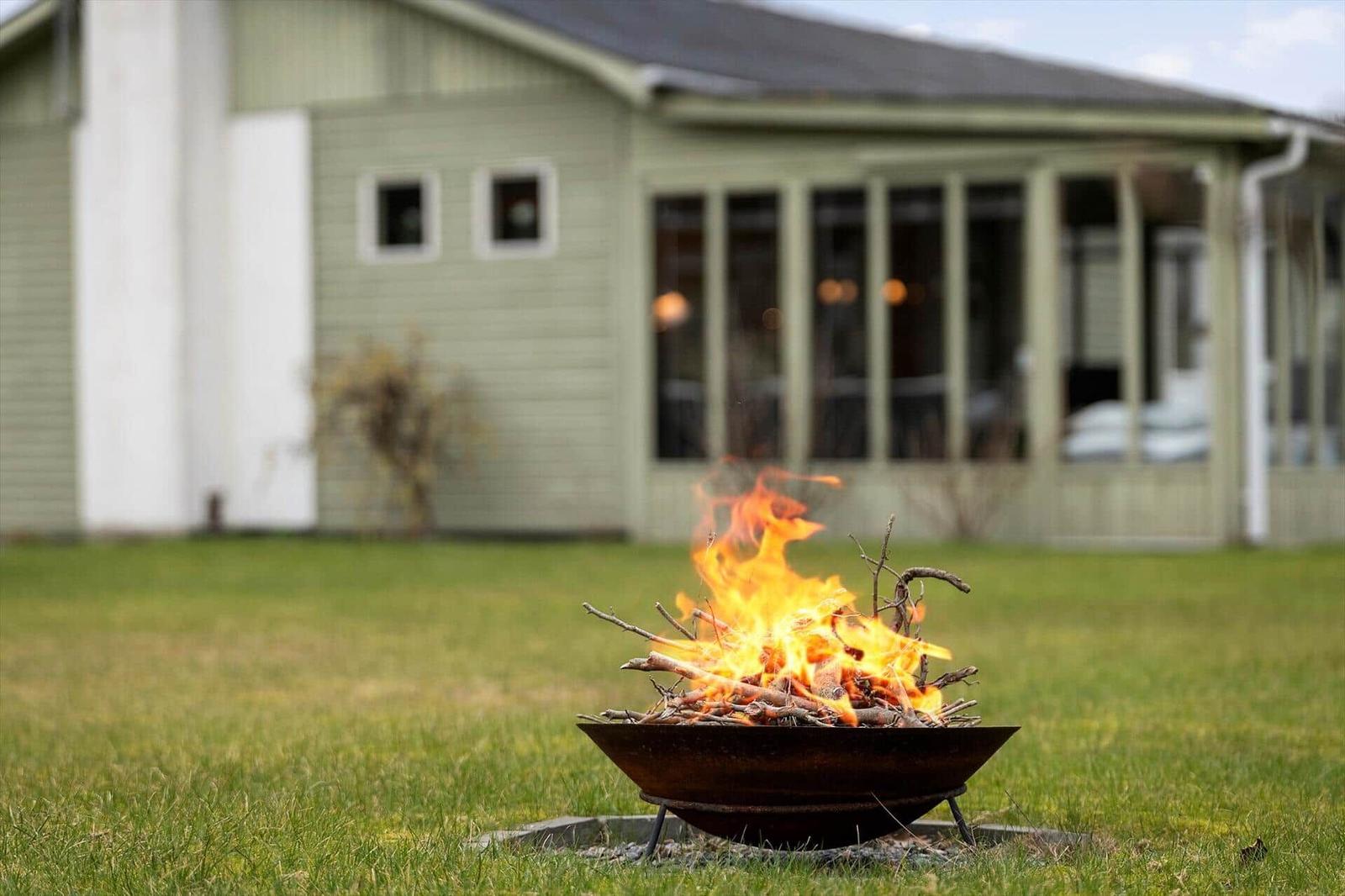 A burning fire pit on a lawn in front of a house with a porch.