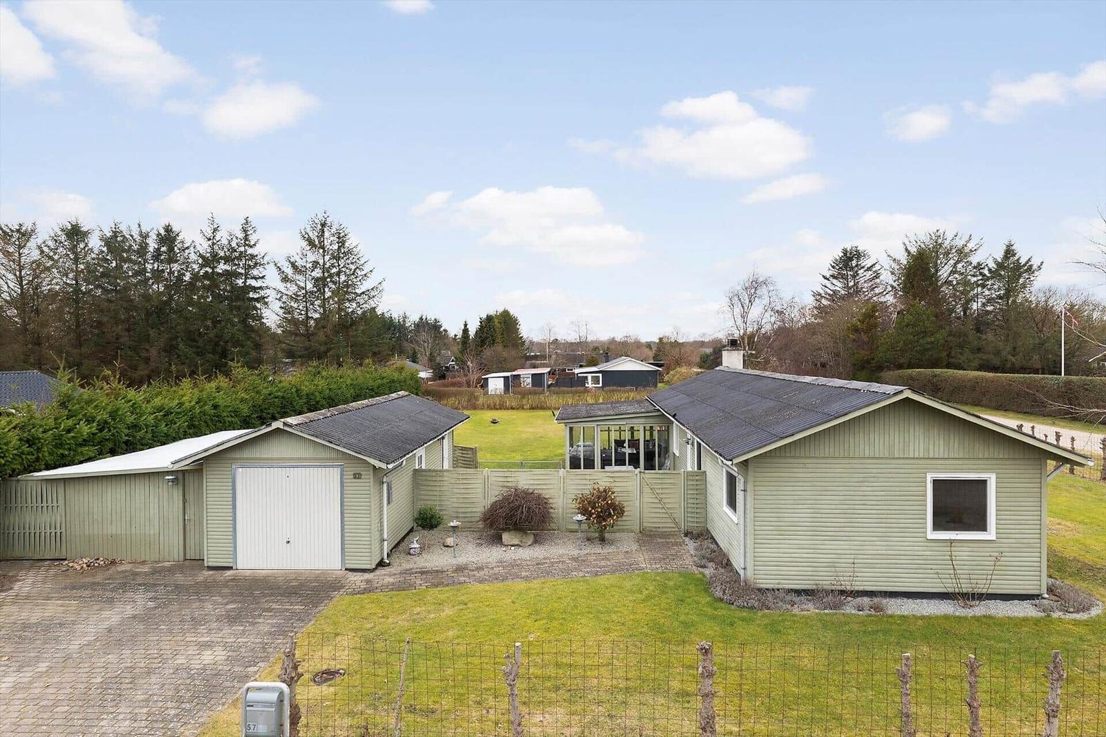 A light green house with a garage and garden. Trees and other houses are visible in the background.