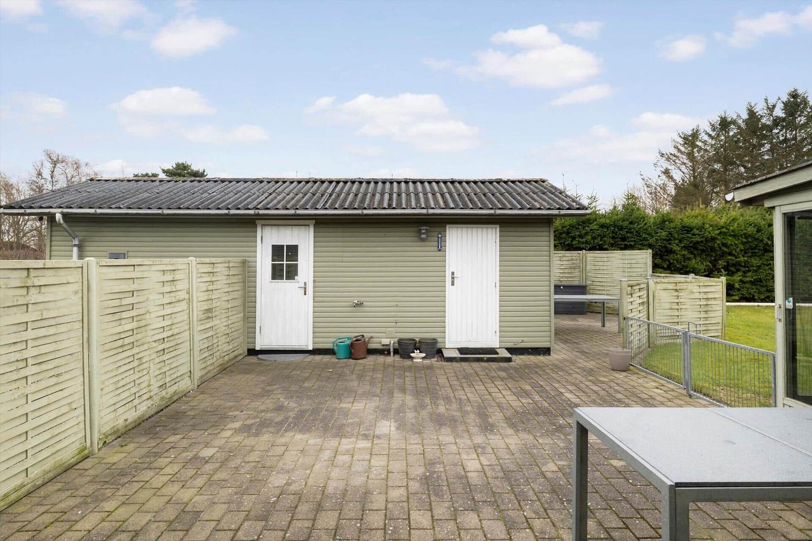 House with patio, fence, and garden. White doors and gray roof tiles.