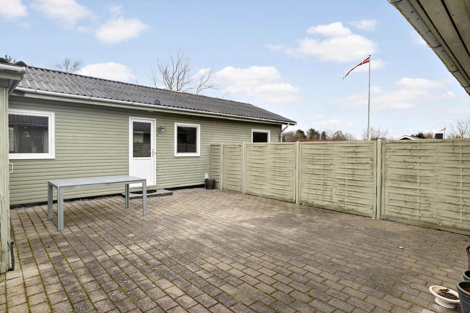 Backyard with patio, table, and Danish flag. Wooden fence and small house.