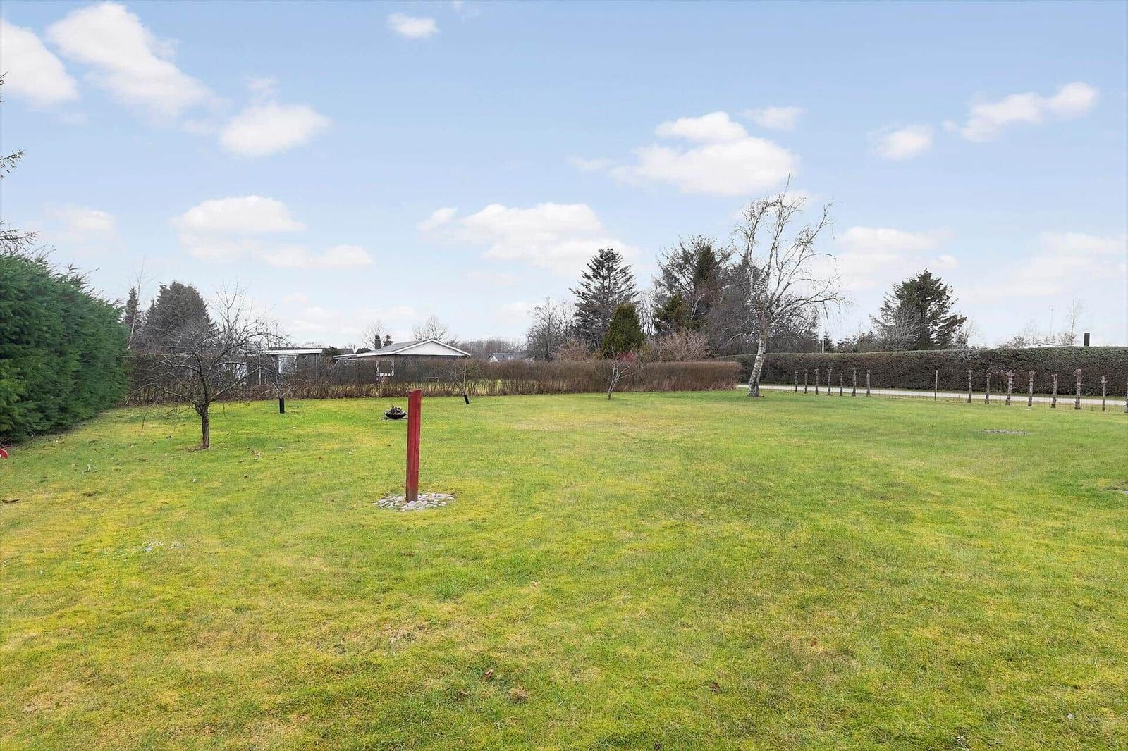 Large green lawn with trees and a red post in the foreground.