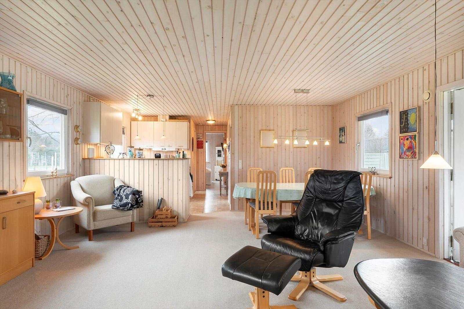Living and dining area with wood paneling and black leather chair.