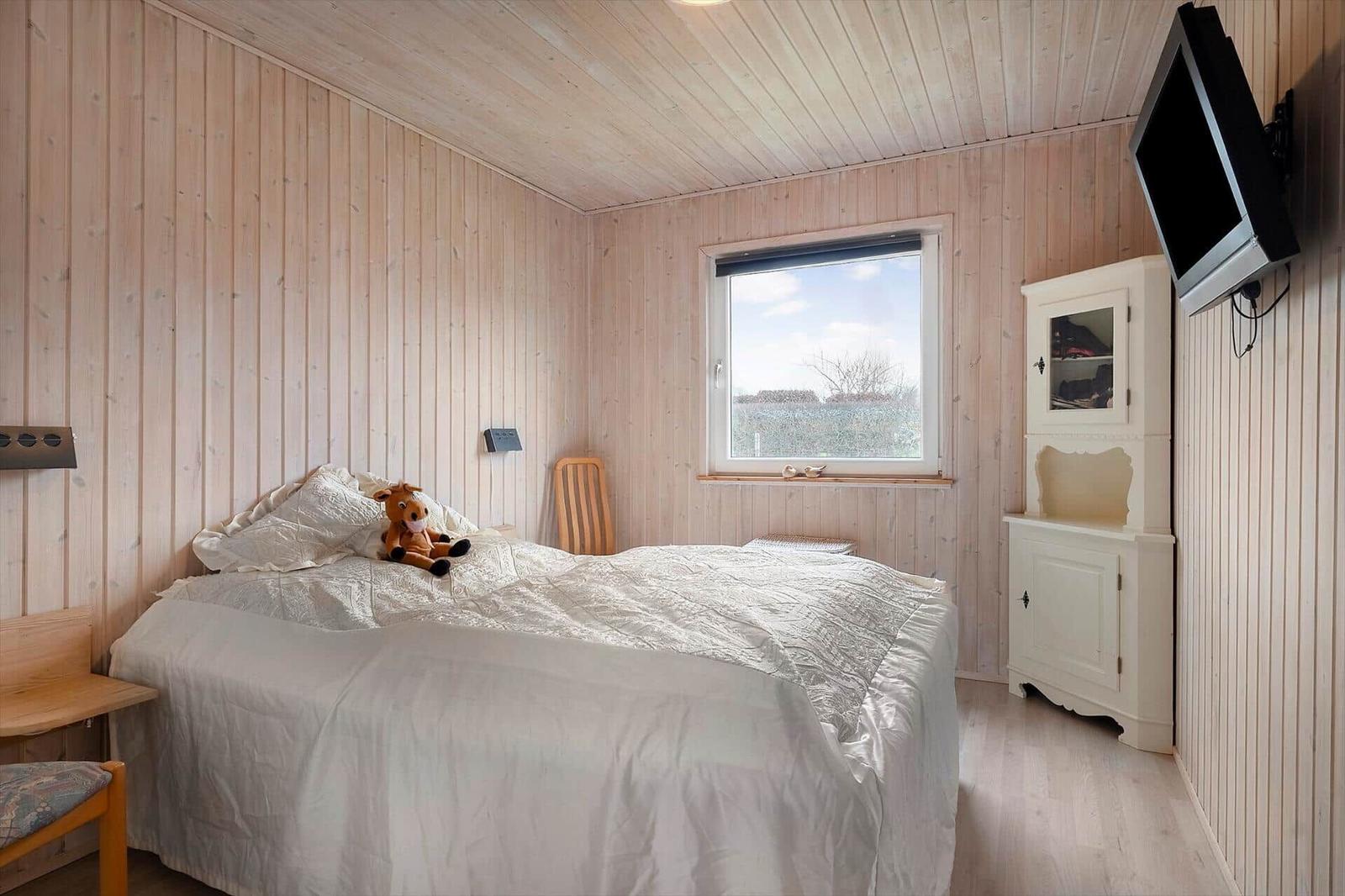 Bedroom with wooden walls, bed, TV, and window.