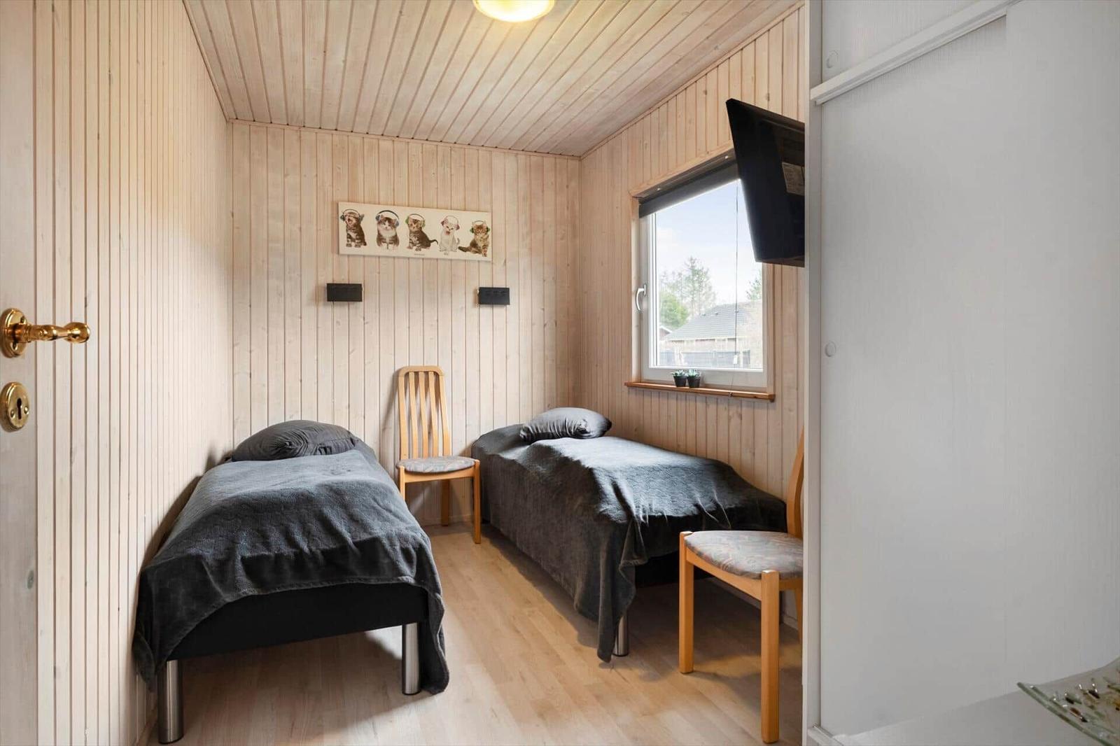 Two beds, wooden walls, window, and TV in a room.