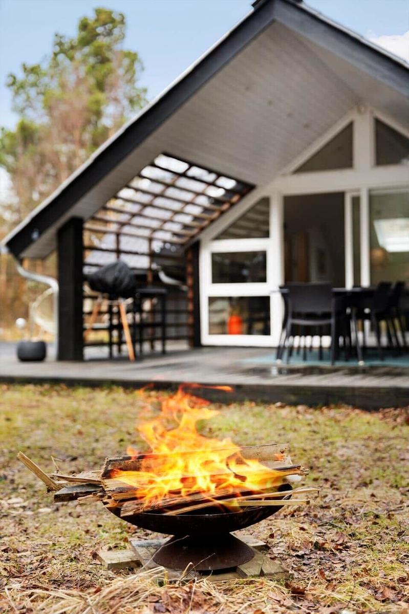 A burning fire pit in front of a modern house with a terrace and seating area.