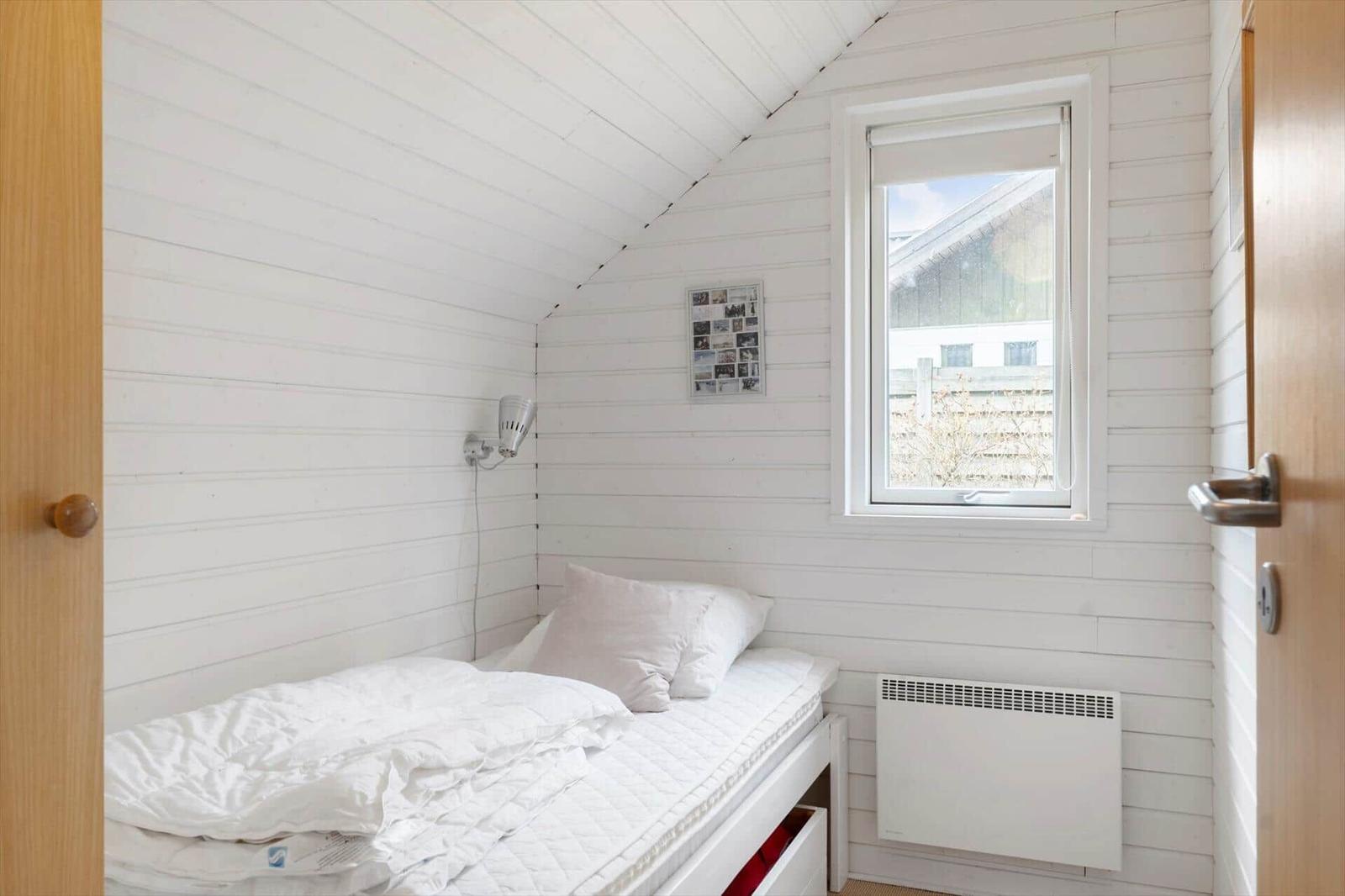 Bedroom with bed, window, and heater against white wood wall.