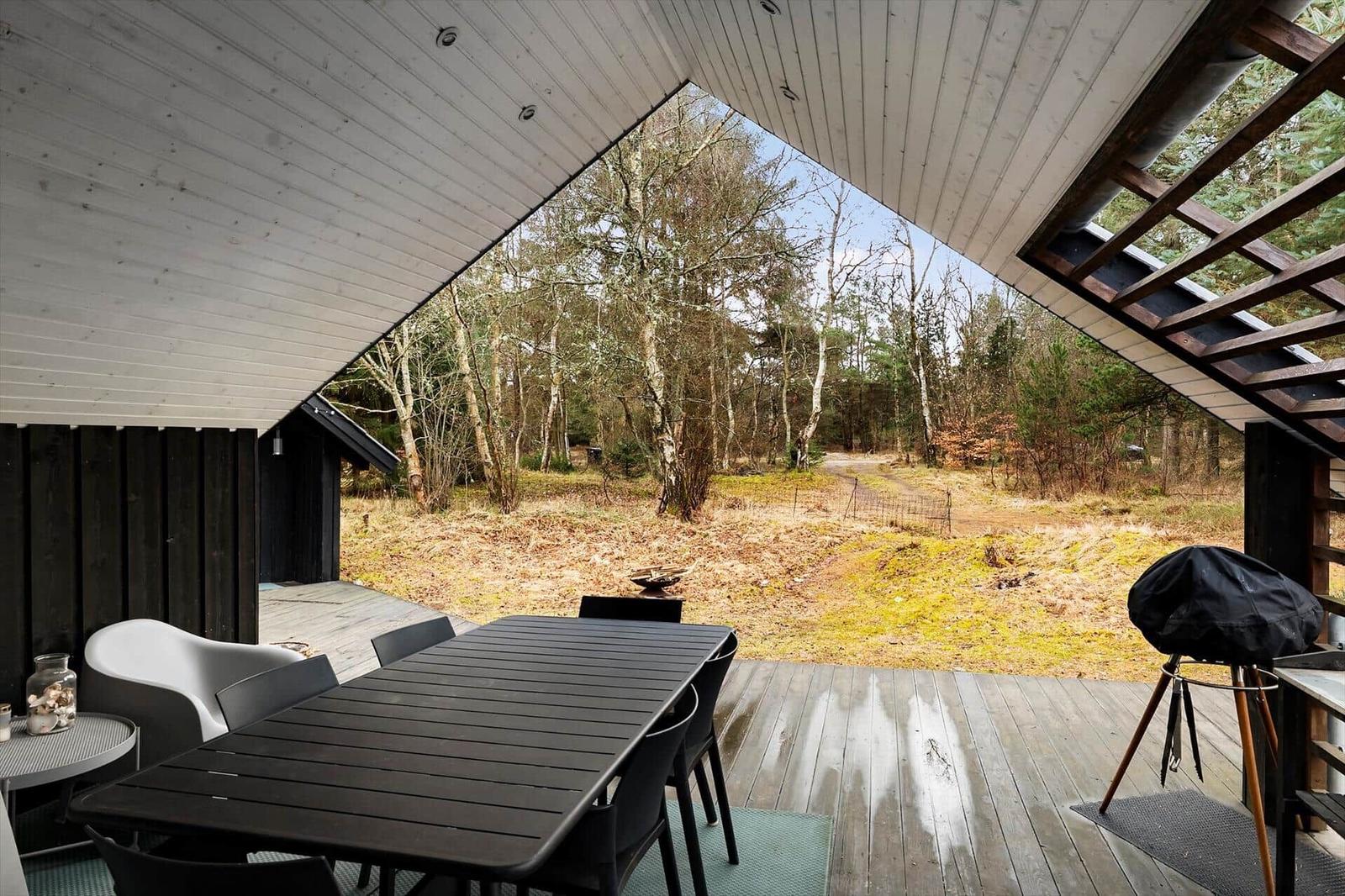Deck with table, chairs, and grill under roof. View into the forest.