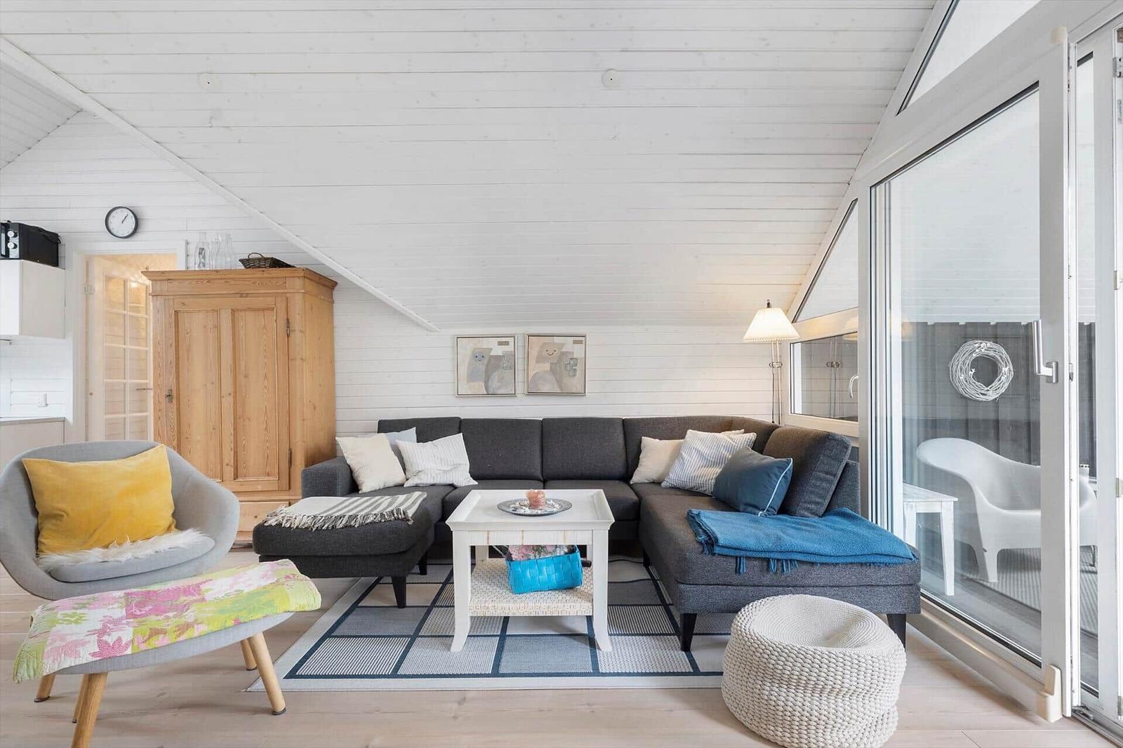 Living room with gray sofa, white table, and wooden wall. Terrace accessible via glass door.