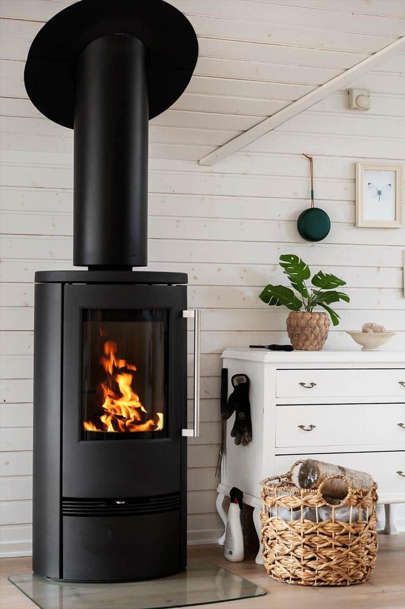 Black wood-burning stove with fire in a room with white wood paneling.