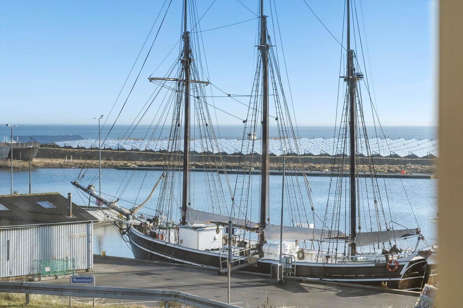 Segelschiffe liegen im Hafen, dahinter sind Solaranlagen und Meer sichtbar.