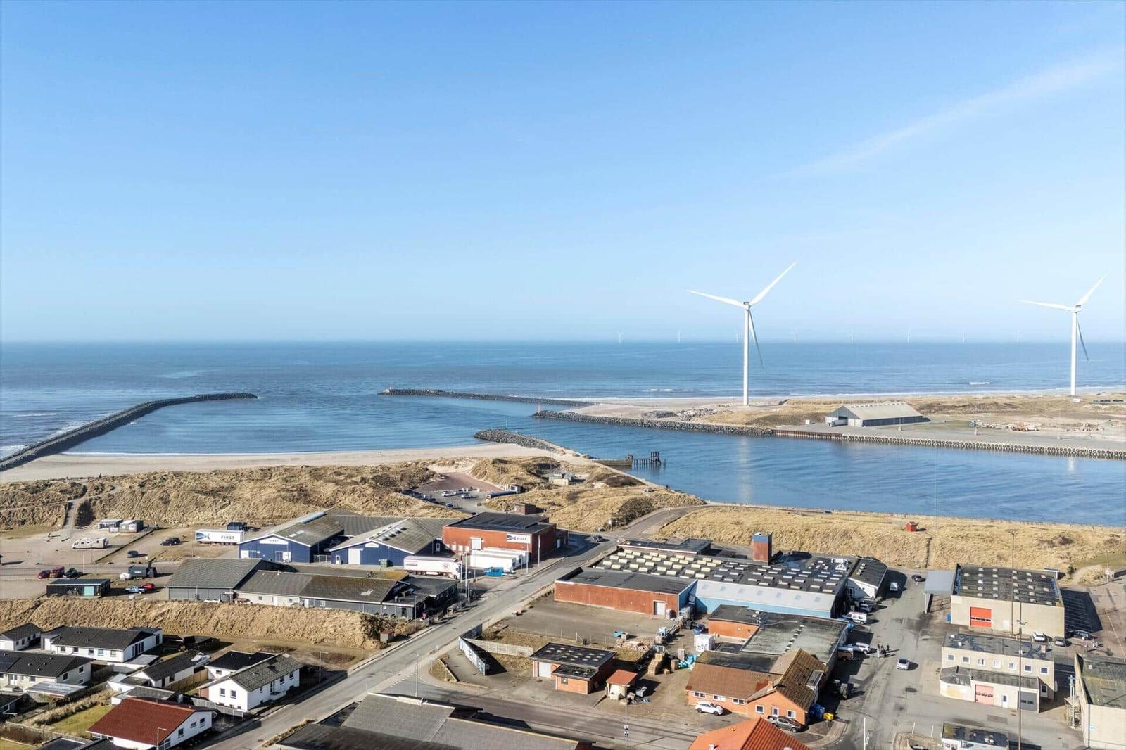 Meer, Windräder und Hafenbereich mit Industriegebäuden und Wohnhäusern.