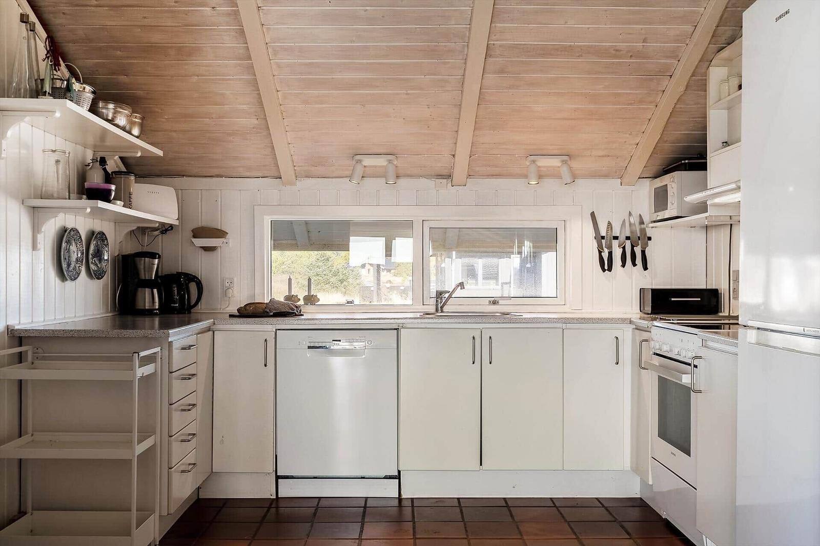 Küche mit weißen Schränken, Spüle, Kühlschrank und Fenstern.