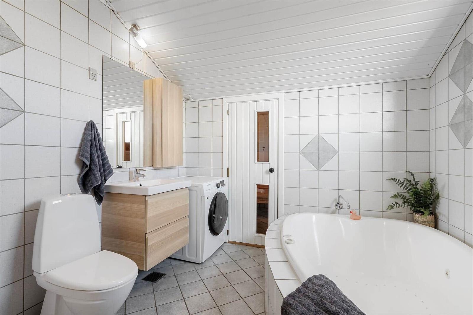 Badezimmer mit Badewanne, Waschmaschine und Toilette.