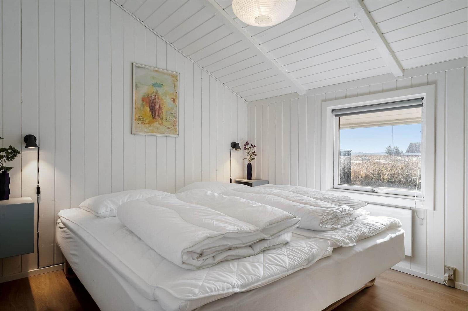 Schlafzimmer mit weißem Bett, Fenster und Holzboden.