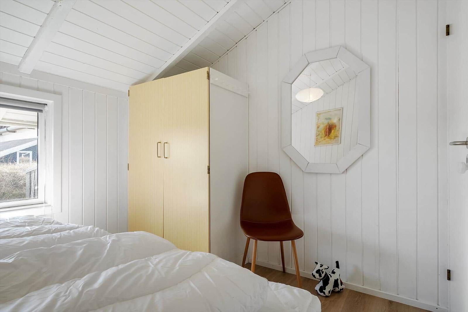 Schlafzimmer mit Bett, Kleiderschrank, Stuhl und Spiegel an der Wand.