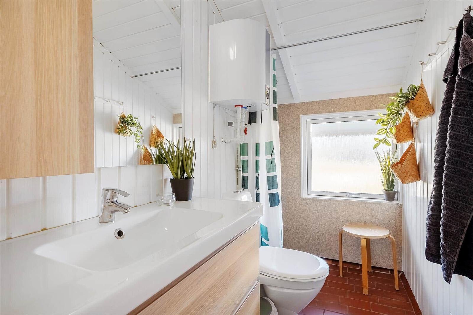 Badezimmer mit Waschbecken, Toilette und Dusche. Holzmöbel, Pflanzen und Fenster.