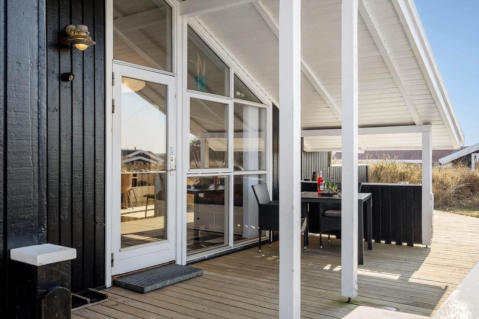 Terrasse mit Tisch und Stühlen unter Dach. Durchgehende Glasfront zur Küche.