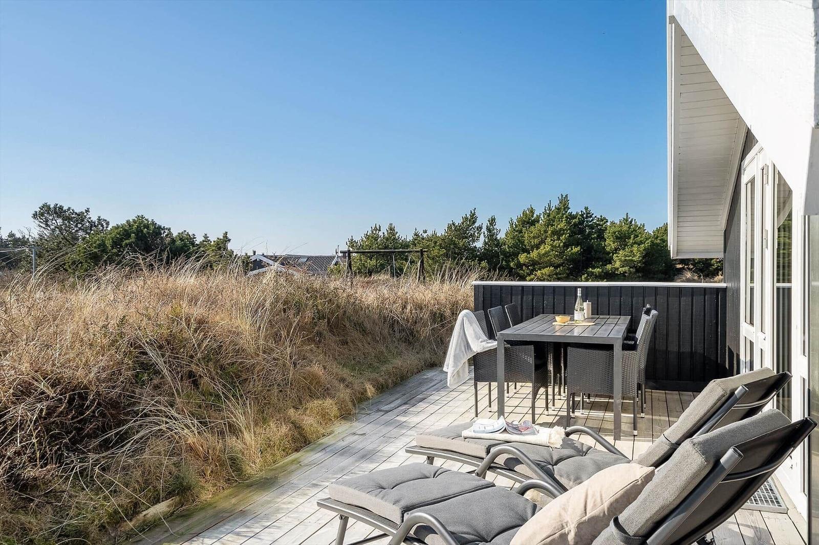 Terrasse mit Loungemöbeln und Esstisch. Blick auf Grasland und Bäume.
