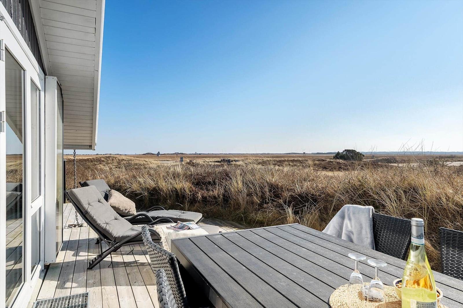 Terrasse mit Tisch, Stühlen und Liegestühlen. Blick auf trockenes Grasland unter blauem Himmel.