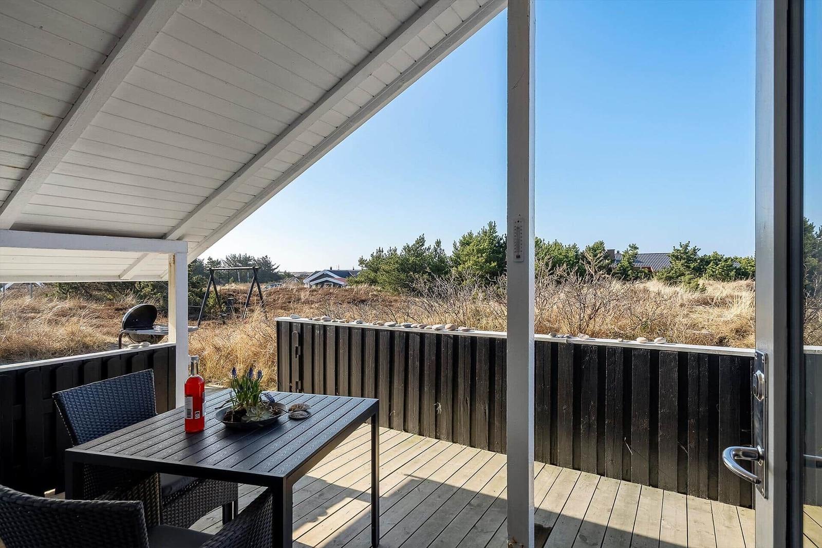 Terrasse mit Tisch, Stühlen und Grill. Blick auf Grasland und Bäume.