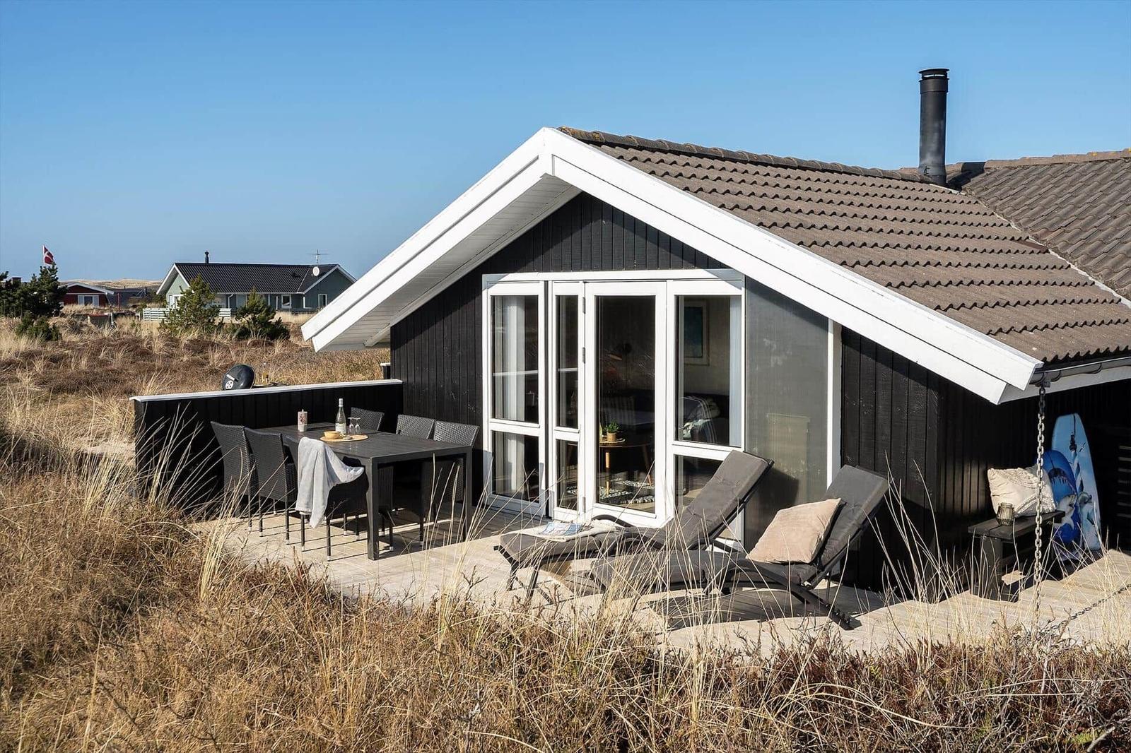 Schwarzes Haus mit Terrasse, Liegen und Grillplatz. Blick auf Strand und Meer.