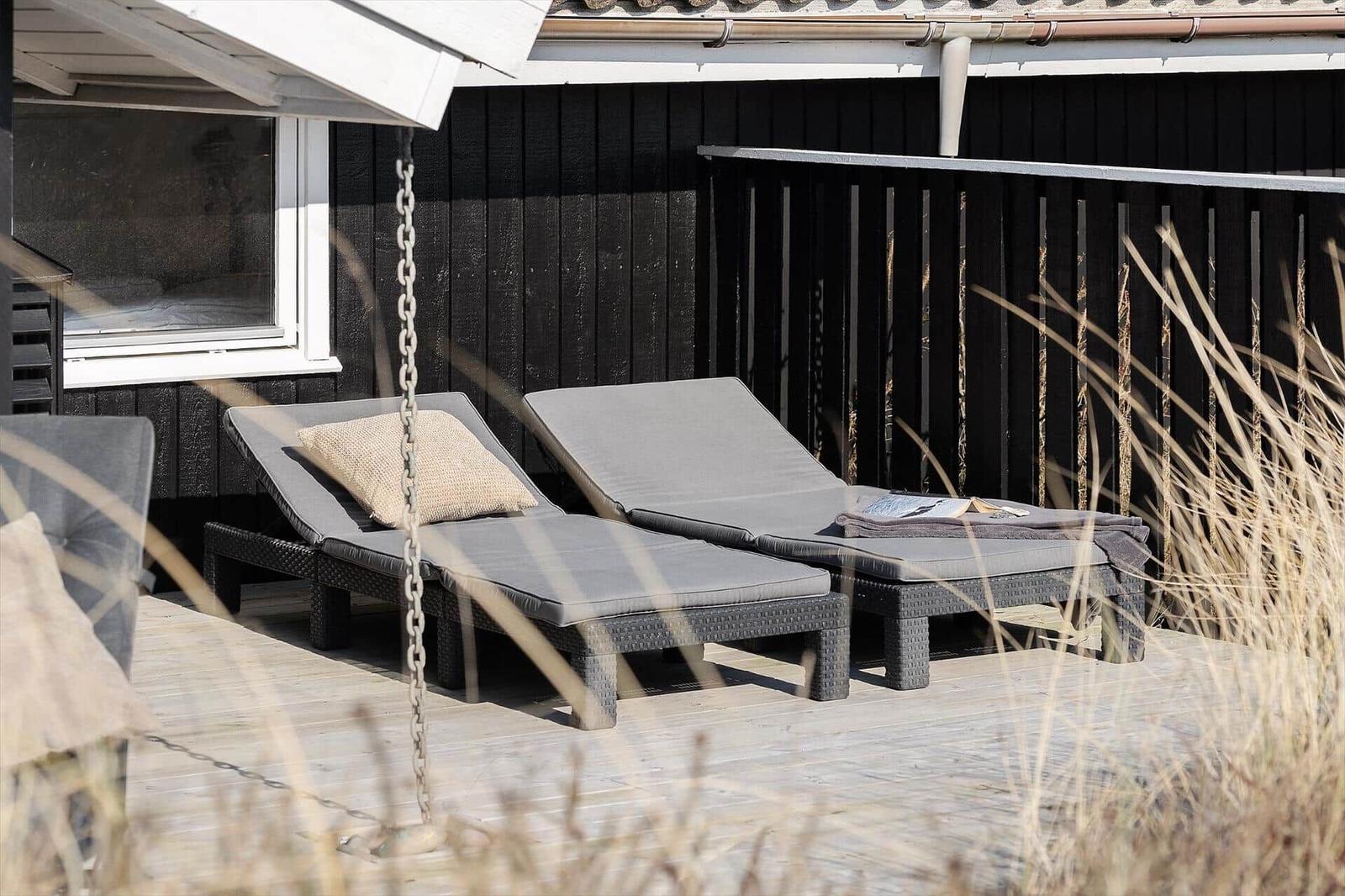 Zwei Liegestühle mit Kissen stehen auf einer Terrasse vor einem Haus.