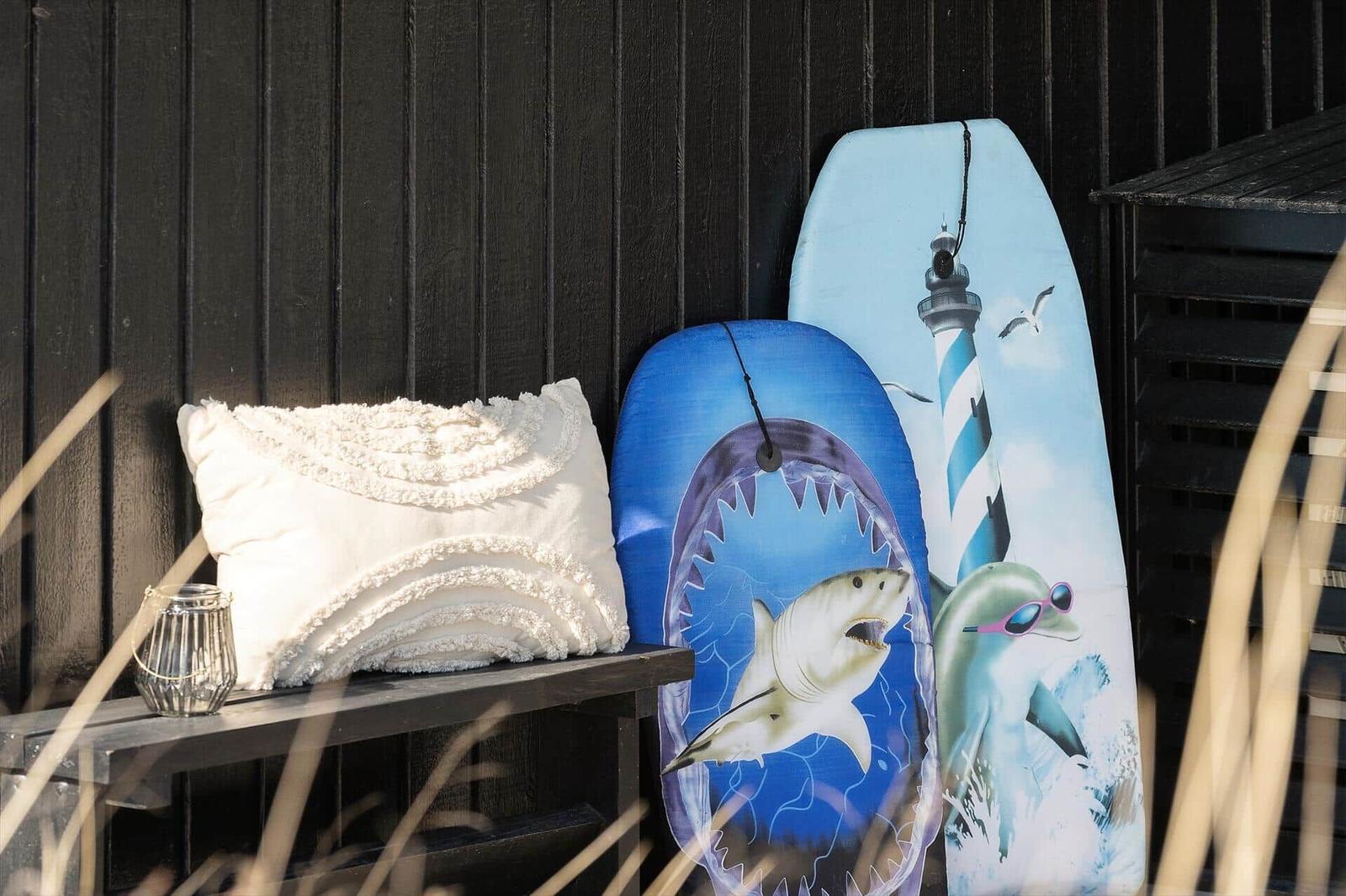 Auf einer Bank stehen Kissen, eine Laterne und zwei Surfbretter mit Meerestieren.