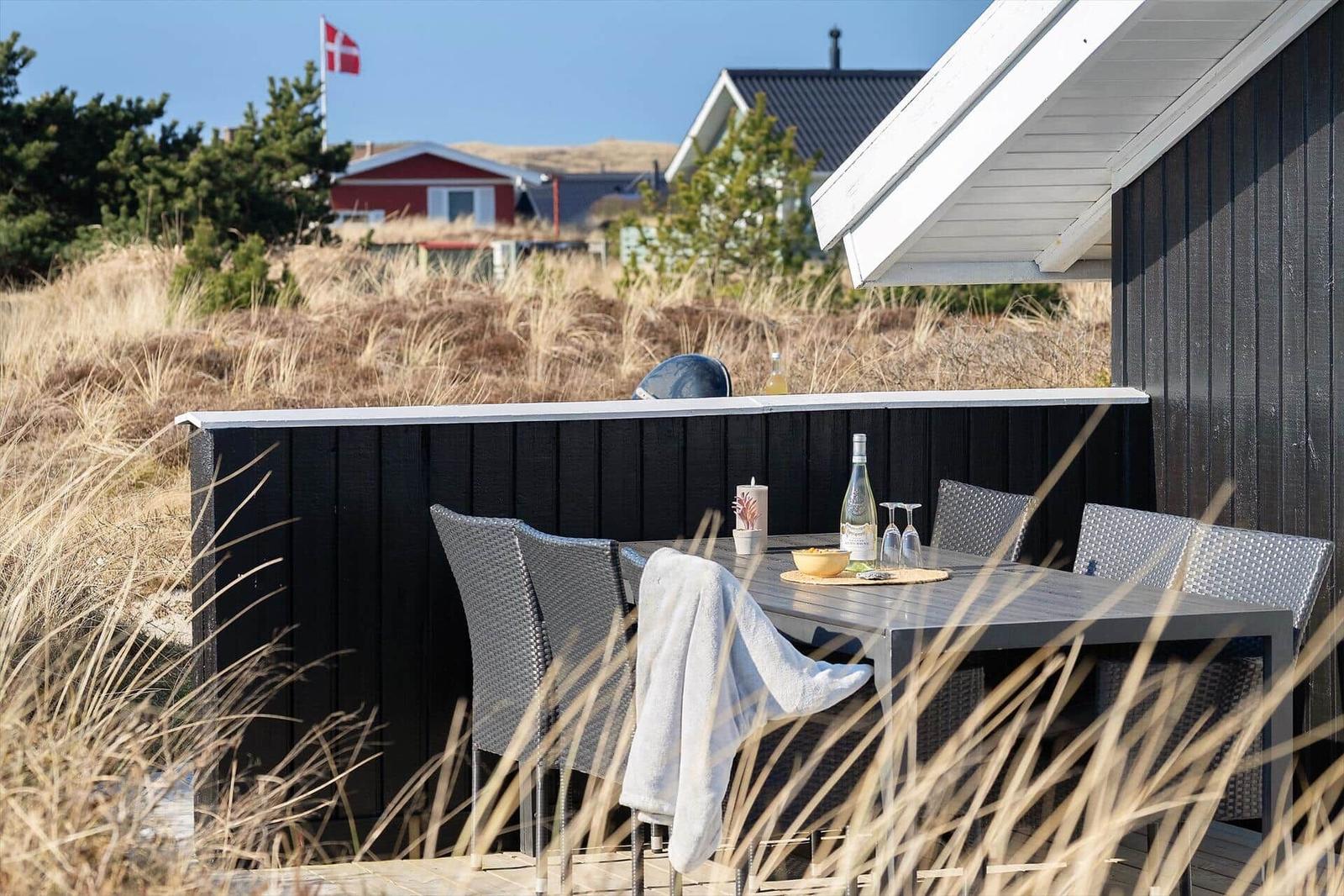 Terrasse mit Tisch und Stühlen, Blick auf Strand und Häuser.