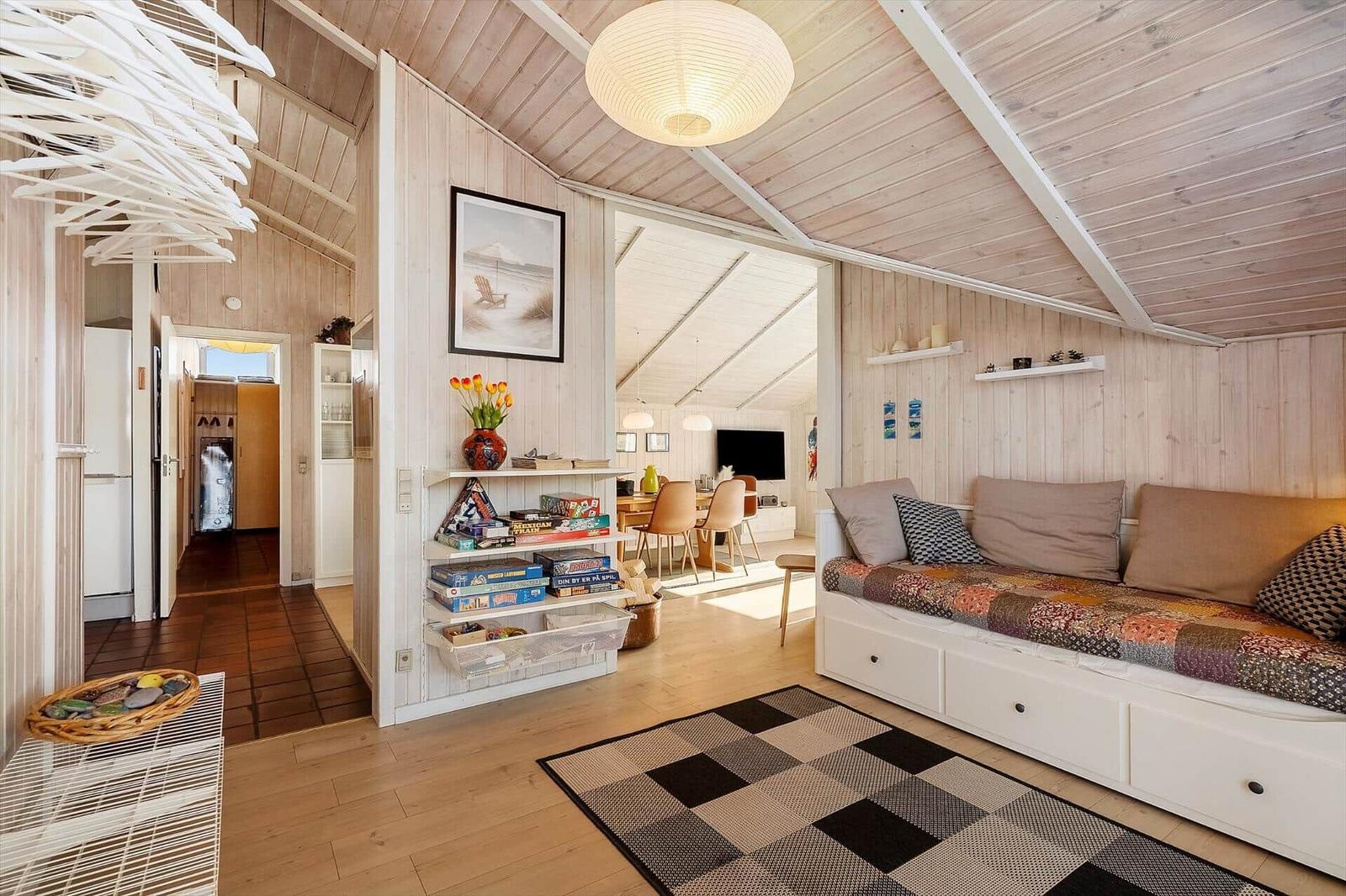 Wohnbereich mit Sofa, Regal und Schlafplatz unter Holzdecke.