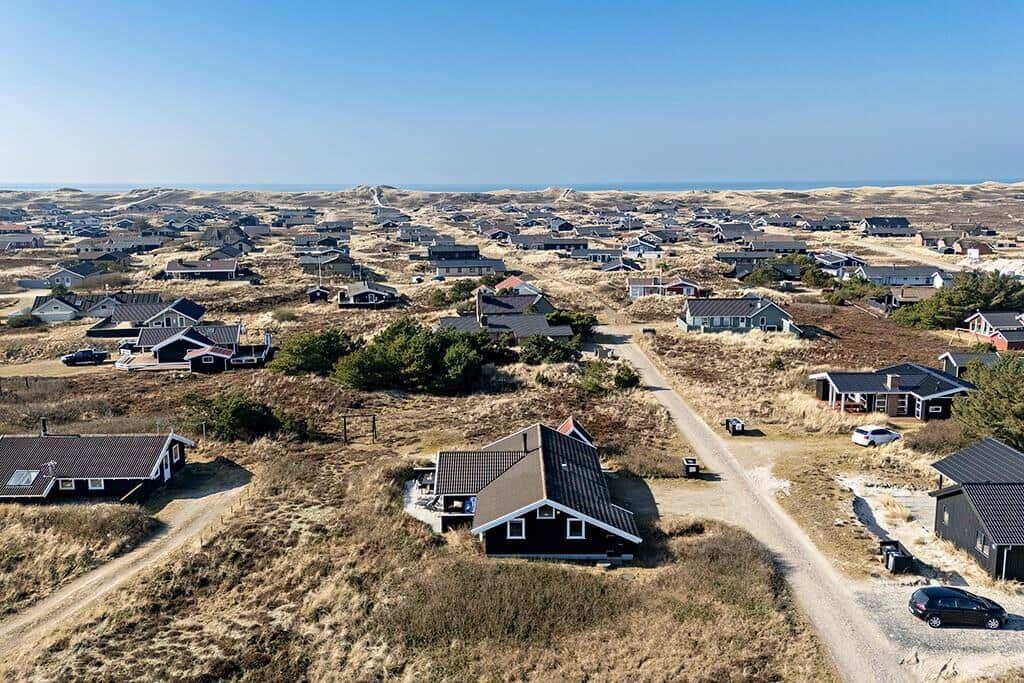 Aerielansicht von Ferienhäusern in einer Dünenlandschaft mit Blick aufs Meer.