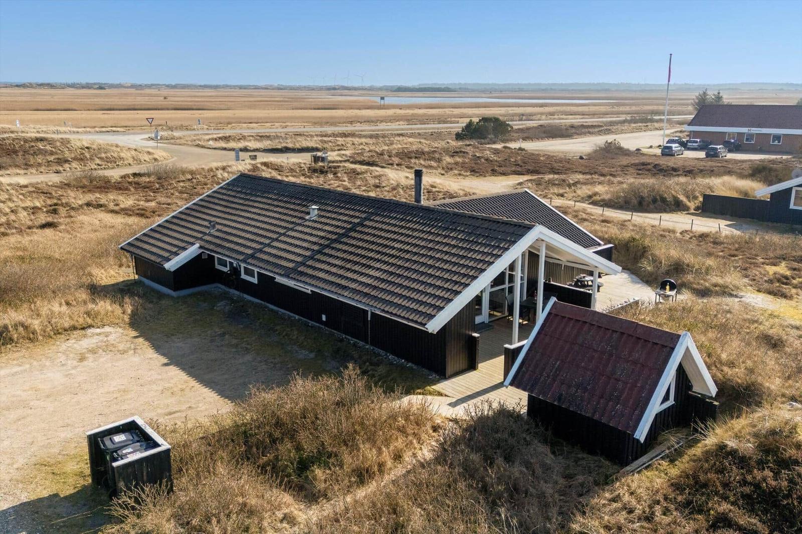 Schwarzes Haus mit Terrasse und kleinem Anbau in einer trockenen Landschaft.